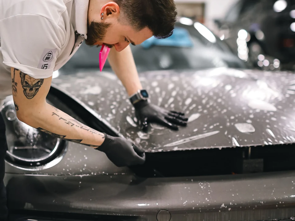 Installer applying wet transparent paint protection film to a vehicle hood