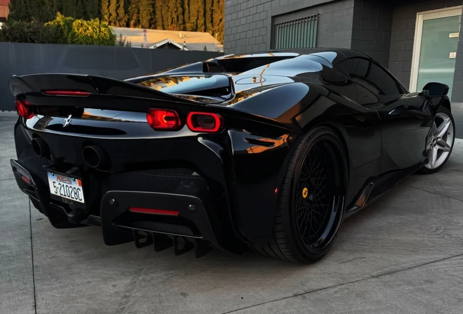 Rear three-quarter view of a gloss black supercar parked outside the shop