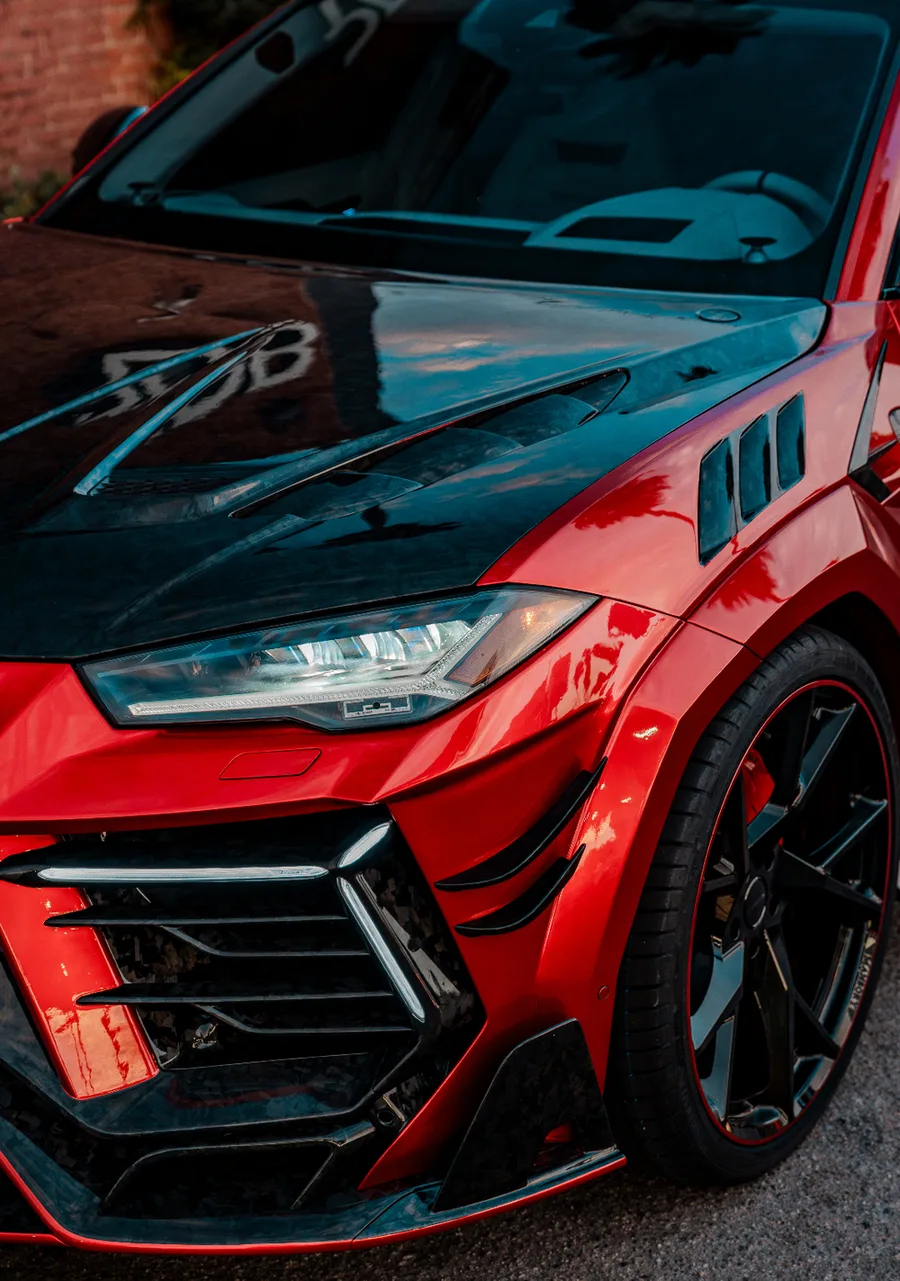 Front three-quarter view of a gloss red widebody SUV with a carbon fiber hood, parked outside a brick building