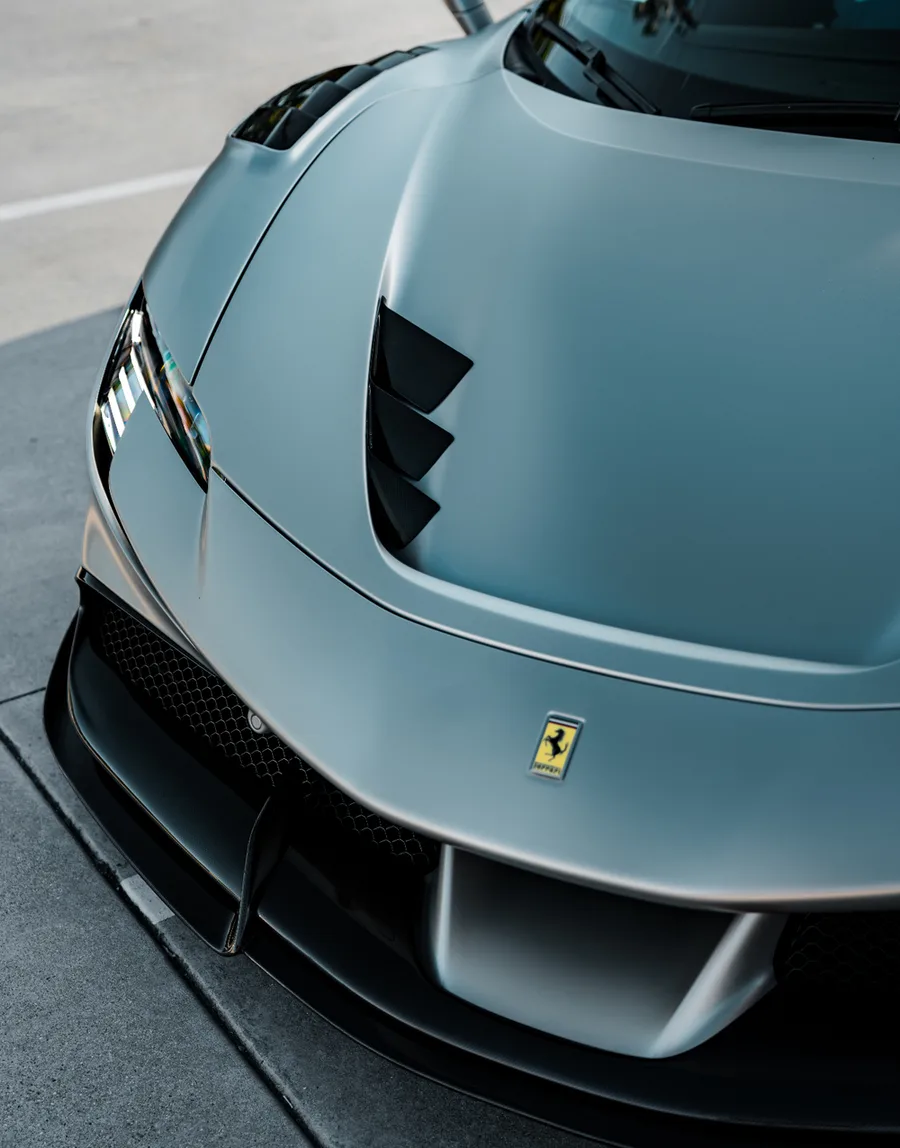 Overhead close view of a matte silver supercar hood with gloss carbon fiber vents
