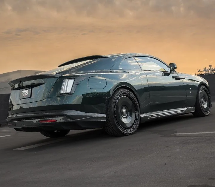 Low rear three-quarter view of a deep metallic green luxury coupe parked on open pavement against a sunset sky