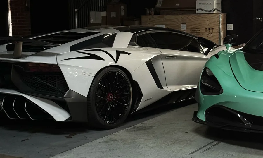 Gloss white supercar with black accents parked beside a mint green supercar inside the workshop