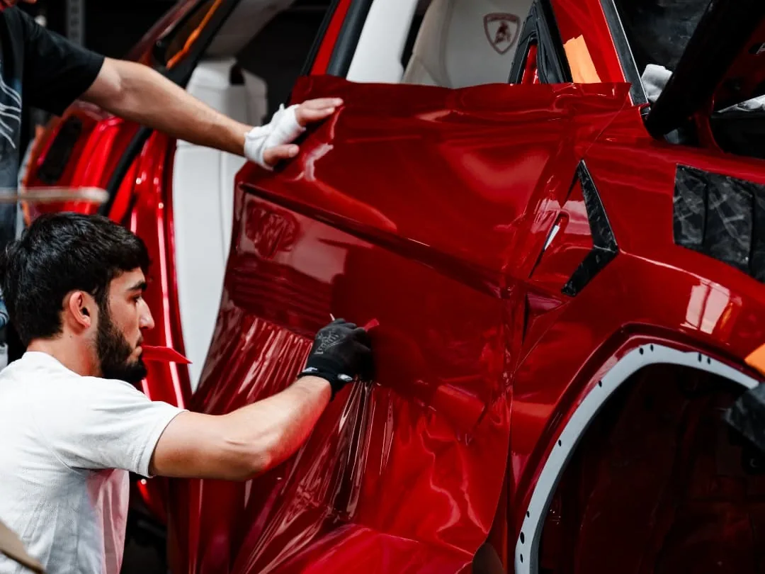 Two installers applying a red vinyl wrap to a car door in the workshop